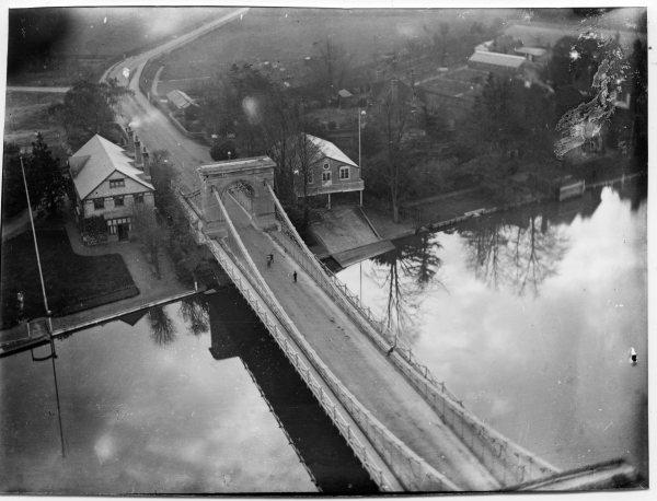 Looking S from the church tower, an elevated view of the carriageway and support columns of the bridge, and adjacent buildings on the bank of the river Thames, Marlow. 1926.