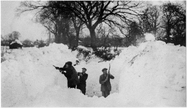 View of men clearing a snowdrift, which is above their heads in depth, with houses in the background, Coleshill. Possibly 1947