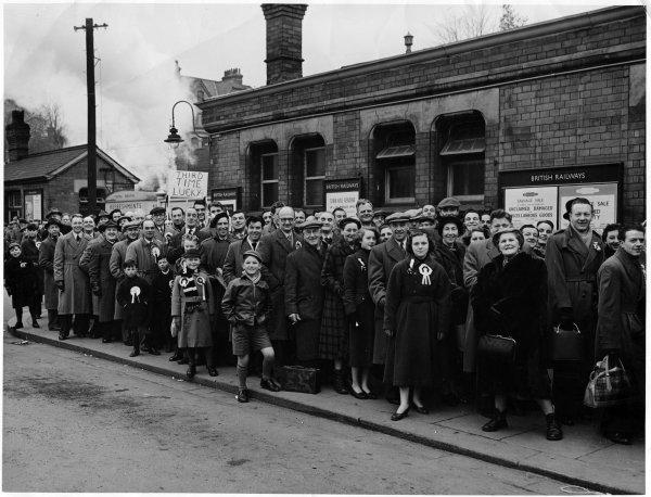 View of a large crowd of smiling people,many sporting rosettes, queueing to board a train, Station Yard, High Wycombe. date unknown