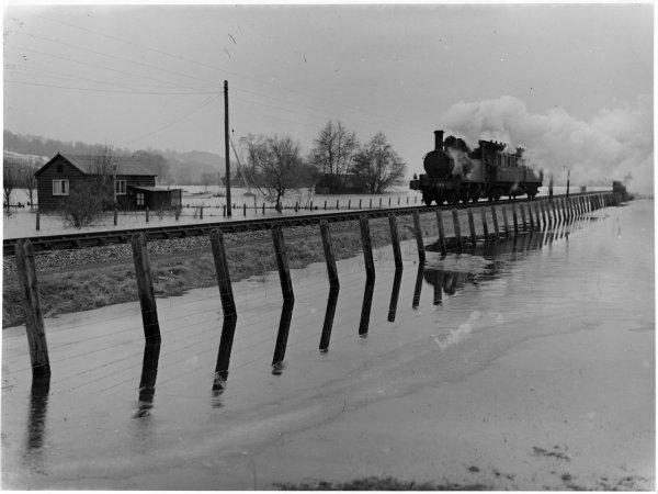 View of the Marlow Donkey steam train, with the fencing beside the track reflected in flood water from the Thames, Spade Oak, Little Marlow. March 1947