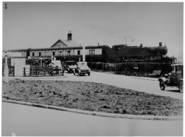 View of the level crossing at the junction of Cores End Rd and Furlong Rd, with cars waiting as a train passes, Bourne End. Circa 1935