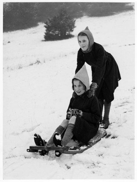 Two girls, one on a sledge the other pushing, playing in the snow on the hill, West Wycombe Estate, West Wycombe. February 1947.