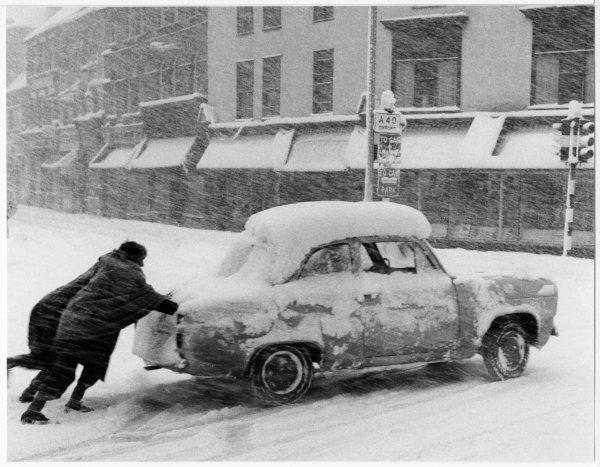 View of two men pushing a car stuck in the snow at the junction of Paul's Row and White Hart St, High Wycombe. December 1961