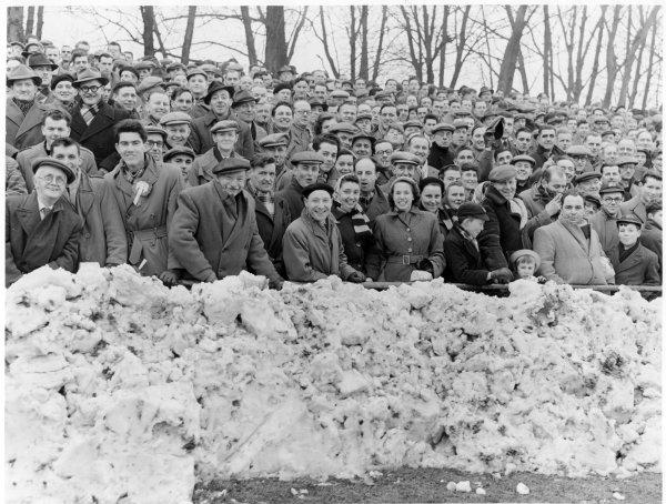 View of the crowd standing behind a pile of snow on the western embankment of Loakes Park for an Amateur Cup match, High Wycombe. February 1955