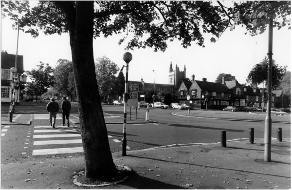 View looking South West cross the roundabout to the parish church, with two men crossing towards the Saracens Head in Beaconsfield in 1975