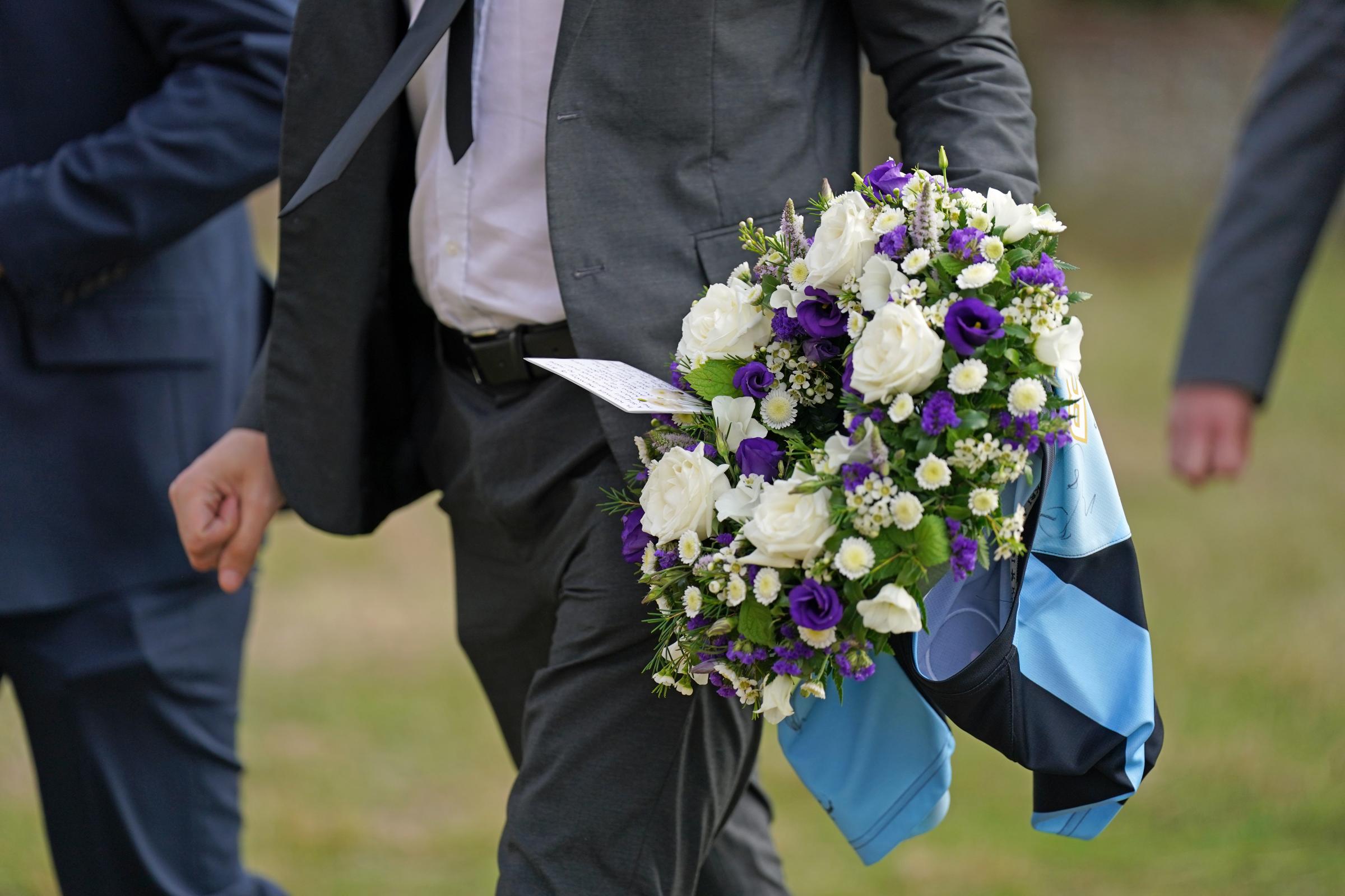 A mourner carrying a bouquet of flowers with a Wycombe Wanderers football shirt arrives for the funeral of TV presenter and journalist Bill Turnbull at Holy Trinity Church in Blythburgh, Suffolk (PA)